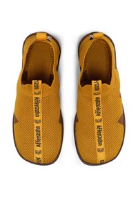 Gelbe Strick-Slip-On-Schuhe mit brauner Sohle, die ein strukturiertes Obermaterial, eine Schlinglasche und kontrastierende Markenbezeichnung über der Ferse aufweisen.