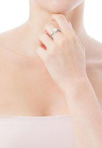 Anello d'argento con una fascia curva e un piccolo accento di perla, mostrato su una mano che tocca il mento. Texture liscia, design minimalista.