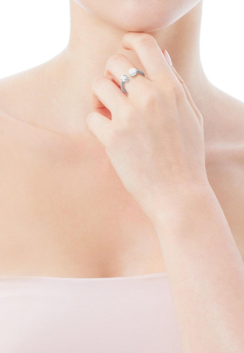 Anello d'argento con una fascia curva e un piccolo accento di perla, mostrato su una mano che tocca il mento. Texture liscia, design minimalista.