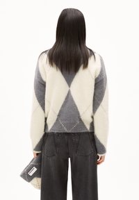 Wollmischpullover mit einem grau-weißen Argyle-Muster, gerippten Bündchen und einem kurz geschnittenen Saum. Kombiniert mit dunkelgrauen weit geschnittenen Hosen.