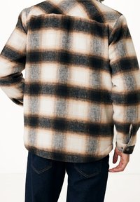 Rutigt skjorta i kräm, svart och rostfärg med en mjuk textur. Har en knäppt manschett och en avslappnad passform. Synliga sömmar och mönster.