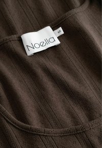 Hnedá ryhovaná tkanina s textúrovaným vzorom. Na výstrihu sa nachádza biela etiketa s nápisom "Noella" a veľkosťou "S".