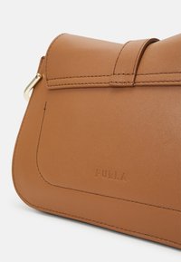 Brown leather handbag with a smooth texture, featuring a stitched design and a gold hardware accent. Embossed brand name is visible.
