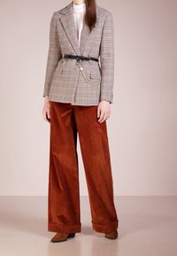 Marynarka w kratę z dopasowaną talią, zestawiona z szerokimi spodniami z sztruksu w kolorze rdzy. Czarny pasek i ozdobny łańcuch podkreślają całość.
