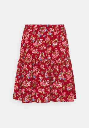 Jupe rouge à fleurs, longueur genoux, avec un niveau froncé, ornée de fleurs roses, bleues et vertes sur un fond uni.