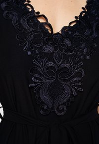 Vestido preto com intrincado bordado azul-marinho em design floral ao longo do decote, com detalhes recortados e cintura amarrada.