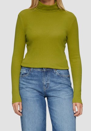 Personne portant un pull vert à col roulé ajusté et un jean en denim bleu taille haute avec des poches avant visibles.