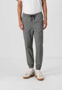 Grijze jogpants met een elastische tailleband, trekkoorddetails, zijzakken en taps toelopende boorden, gecombineerd met witte sneakers.