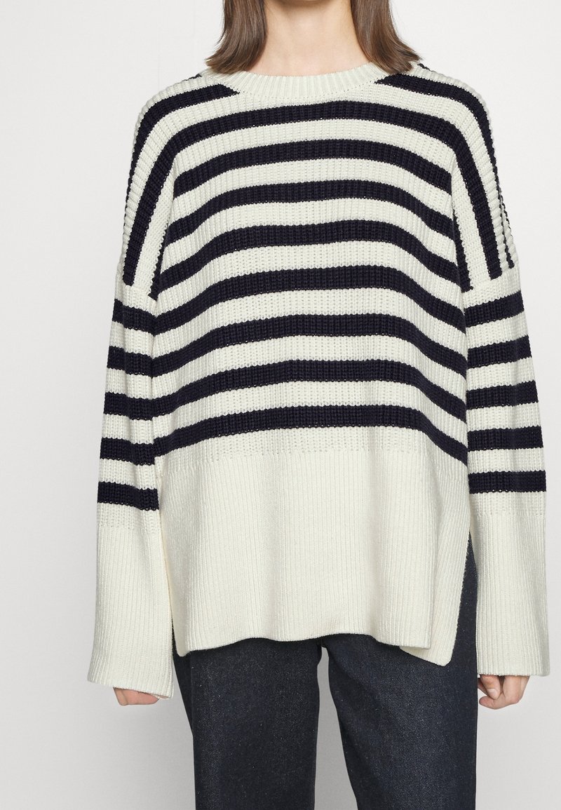 Knitted sweater with wide navy stripes on a cream background, featuring a crew neck, loose fit, and ribbed texture.