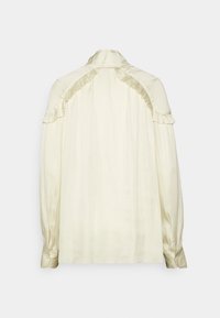 Kremowa satynowa bluzka z długimi bufkami, falbanką na karku i ramionach oraz mankietami na guziki.