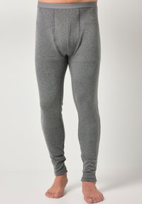 Mann trägt eng anliegende graue Thermo-Leggings und steht barfuß vor einem schlichten weißen Hintergrund.