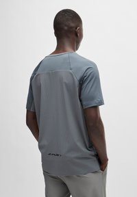 T-shirt de sport gris à manches courtes, avec un dos en maillage, un devant lisse, une coupe ample et un logo discret près de l'ourlet.