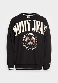 Felpa nera in cotone con maniche lunghe, con testo bianco e dorato "TOMMY JEANS" e un logo con bandiere. Presenta polsini a costine.