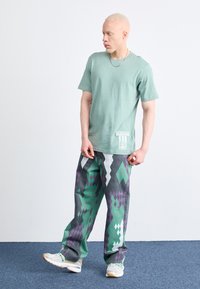 Világoszöld pamut póló, kicsi fehér Adidas logóval, laza, mintás szürke nadrággal párosítva, zöld és lila rombusz formákkal.