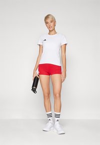 White athletic t-shirt with black logo, red shorts, black water bottle, white sneakers, and striped socks. Smooth fabric, fitted design.
