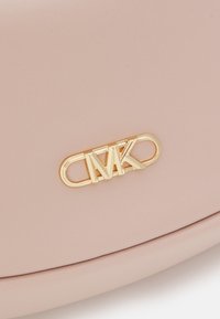 Jasnoróżowy syntetyczny materiał o gładkiej teksturze z wyraźnym akcentem w postaci złotego logo "MK", umieszczonym na przodzie.