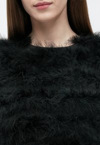 Sort faux pels top med et tekstureret, lagdelt design med bløde, fluffy tråde. Halsudskæringen er rund, og den overordnede form er tætsiddende.