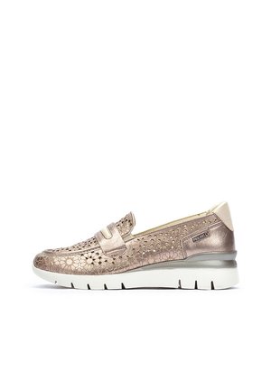 Zapato slip-on de bronce metálico con diseño perforado, correa acolchada, suela blanca contrastante y punta redondeada, presentando una textura suave.