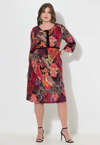 Rotes Kleid mit Paisley-Muster, Drei-Viertel-Ärmeln, runder Ausschnitt und schwarzen Samtakzenten in der Taille. Glatter Stoff, knielanges Design.