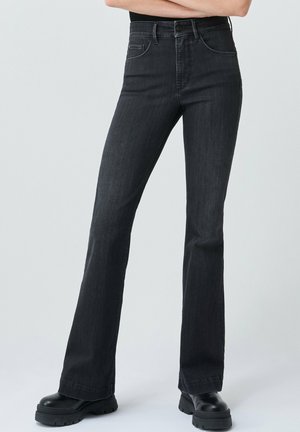 Jean flare noir taille haute, en denim. Avec poches avant et détails de couture. Associé à des bottes noires imposantes.