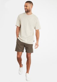 Lys beige t-shirt med korte ærmer og rund hals, parret med olivengrønne shorts og hvide sneakers. Enkel design, casual pasform.