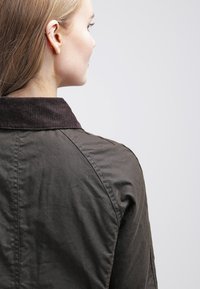 Brown jacket with a corduroy collar, featuring a textured fabric and structured shoulder seams. View is from the back.