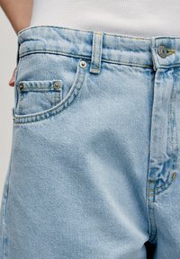 Lichtblauwe spijkerbroek met een klassieke vijf-pocketontwerp, subtiele vervaging, contrast stiksel en een metalen knoopsluiting aan de tailleband.