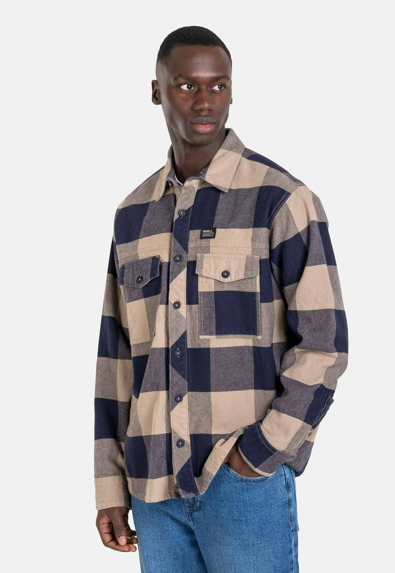 Camisa de franela a cuadros en beige y azul marino, con un frente abotonado, dos bolsillos en el pecho y un corte recto. Textura suave con un diseño clásico.