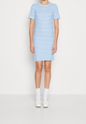 Osoba stojąca w niebiesko-białej sukience w poziome paski, o długości do kolan, z krótkim rękawem, w białych skarpetkach i kremowych butach typu Mary Jane.