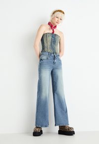 Denim corset top with vertical seams, paired with light blue wide-leg jeans. Platform shoes have a leopard print. Red neck scarf accentuates look.