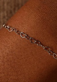 Zilveren kettingarmband met ovale schakels op een donkere huid achtergrond, die een gladde, gepolijste afwerking en een delicaat ontwerp toont.