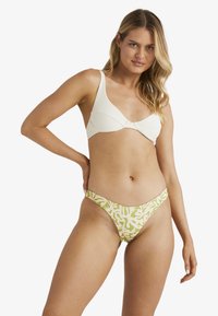 Bikini souprava s texturovaným bílým topem s detailním kroucením a nízkými zelenými kalhotkami s abstraktním bílým vzorem.