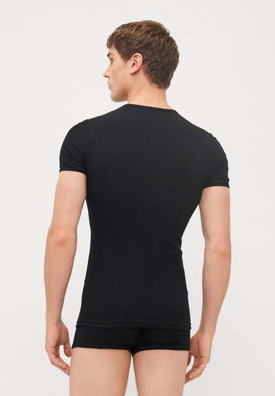 Schwarzes, figurbetontes T-Shirt aus elastischem Stoff, mit kurzen Ärmeln, glatter Textur und Rundhalsausschnitt. Die Ansicht zeigt das Detail auf der Rückseite, kombiniert mit passenden Shorts.