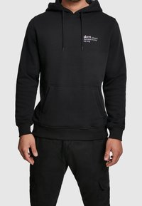 Felpa nera con cappuccio realizzata in tessuto morbido, dotata di tasca a marsupio frontale, cappuccio con coulisse regolabile e piccolo dettaglio testuale bianco sul petto.