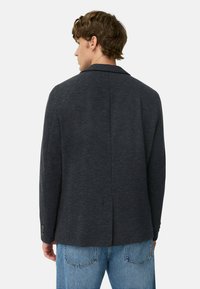 Ciemnoszary żakiet o teksturowanym materiale, slim fit, z klapami i zapinanymi mankietami, w połączeniu z jasnoniebieskimi dżinsami.