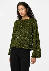 Top lungo a maniche, verde con paillettes, dal fit rilassato e scollatura ampia. Superficie texture con dettagli lucidi e riflettenti. Abbinato a pantaloni neri.