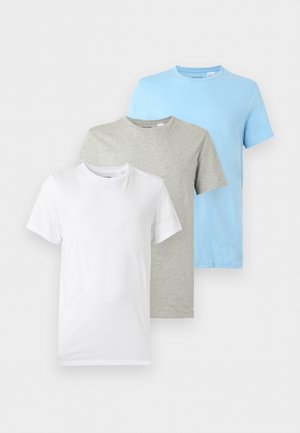 Mann står barfot iført en lys grå kortermet t-skjorte og matchende shorts foran en ensfarget hvit bakgrunn.