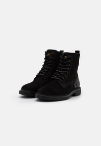 Botines de ante negro con cordones, suelas de goma y puntera redondeada; presentan una parte superior texturizada y detalles de costura.