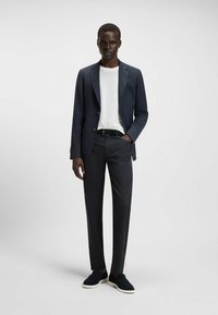 Marineblauwe op maat gemaakte blazer met twee knopen over een wit T-shirt, gecombineerd met zwarte broek en marineblauwe instappers. Glad texturen overal.