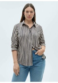 Gestreepte blouse in beige en zwart, met een knoopsluiting aan de voorkant, kraag en opgerolde mouwen. Gepaard met lichtblauwe denim jeans.