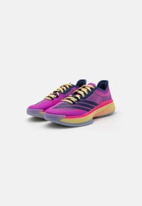 Scarpe sportive con una vivace tomaia in mesh rosa, lacci gialli e una suola sfumata. Presentano tre strisce scure sul lato e un design testurizzato.
