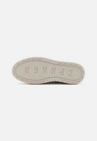Sålen av en sneaker, med et teksturert gummimateriale i off-white, med en hevet logo og sykluskjermmønster rundt kanten.