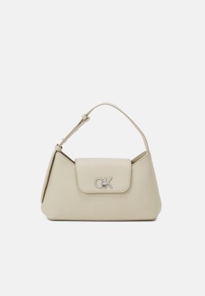 Sac à main beige porté épaule avec fermeture à rabat et logo CK argenté sur le devant, avec une bandoulière simple réglable sur fond uni.