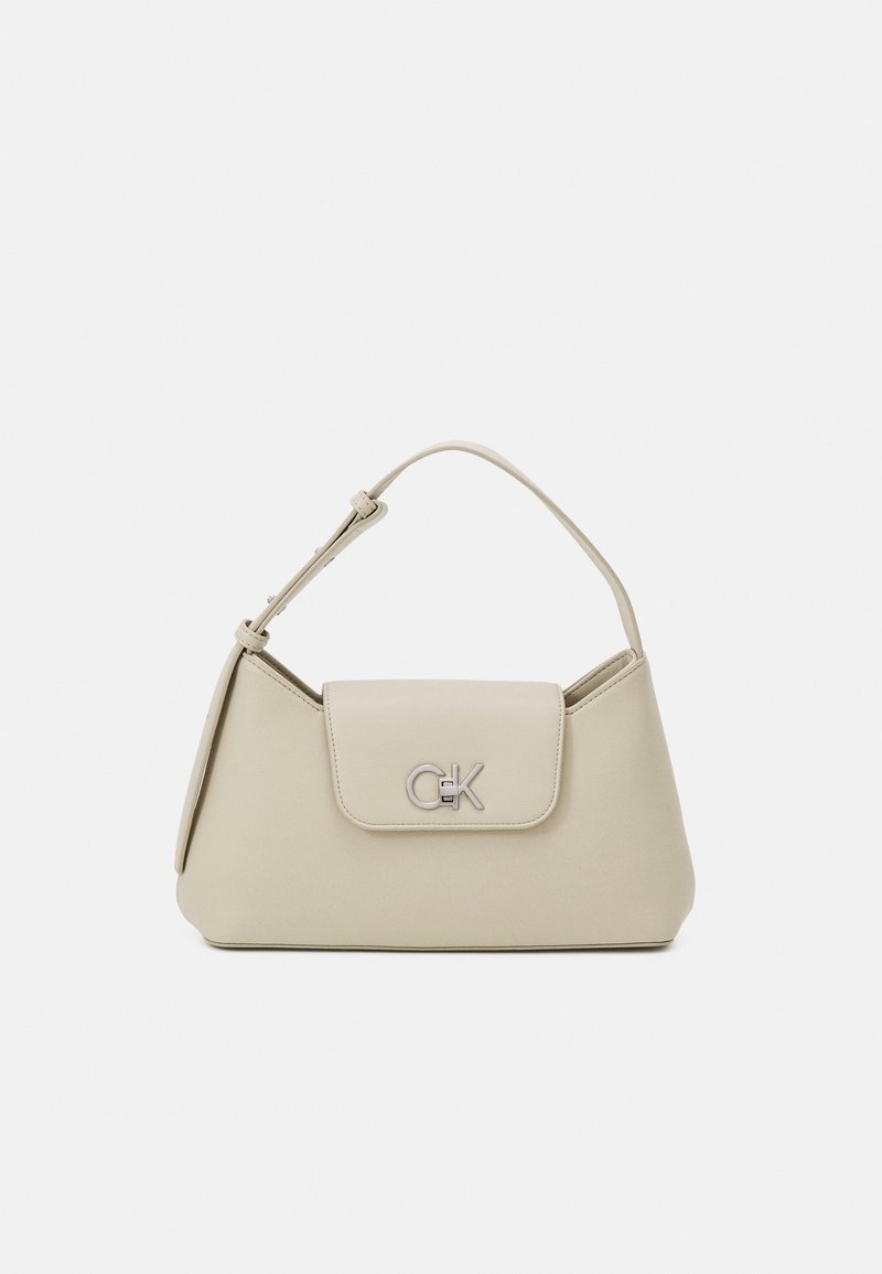 Sac à main beige porté épaule avec fermeture à rabat et logo CK argenté sur le devant, avec une bandoulière simple réglable sur fond uni.