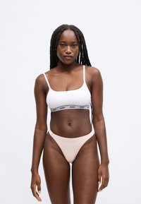 Bijeli kroptop s crnim remenom "HUGO", uparena s blijedo ružičastim tangama. Glatki materijal; minimalistički dizajn; tanke naramenice.