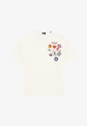 T-shirt de algodão branco com vários emblemas coloridos, incluindo texto e gráficos como um crânio, uma cobra e bandeiras nacionais. Mangas curtas, gola redonda.