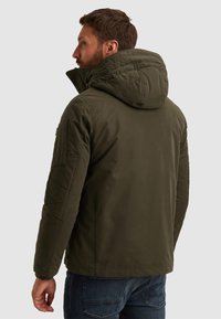 Tmavě zelená prošívaná bunda s velkou kapucí, zobrazená zezadu. Má prošité detaily a boční kapsu na levém rukávu.