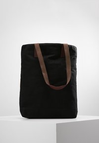 Sac fourre-tout en toile noire avec des sangles en cuir marron, forme rectangulaire, texture douce, sans logos ni ornements visibles.