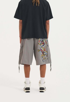 Black cotton t-shirt paired with gray cargo shorts featuring colorful dragon embroidery. Sneakers with white socks complete the look.