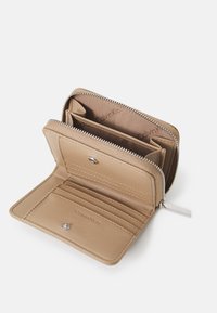 Cartera de cuero beige con cierre de cremallera, múltiples compartimentos para tarjetas y un interior forrado con el nombre de la marca. Diseño simple y compacto.